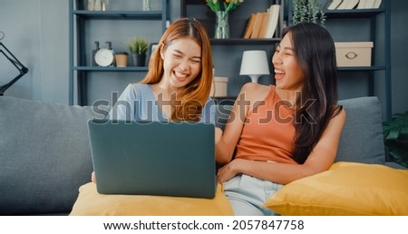 Two Asia lesbian women site on couch together looking at laptop screen in living room at home together. Happy couple roommate ladies enjoy web surfing online shopping, Lifestyle woman at home concept.