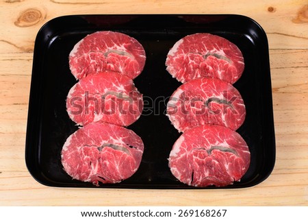Raw beef chuck eye in black tray on wooden background.