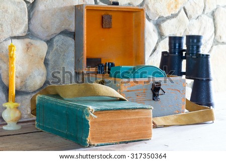 old book measuring device in a wooden case, binoculars and wax candle near a stone wall closeup, vintage style and concept of research and study