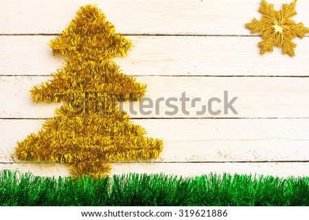 gold Christmas decoration in the form of a Christmas tree, snowflake in the sun and green tinsel in the form of grass, on white wooden boards