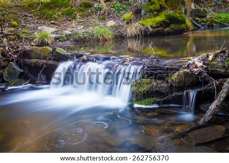 Small waterfall on creek flowing over the rocks and wood