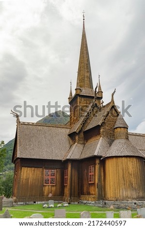Lom viking medieval stave church in Lom Norway. Old wooden walls and tower, green lawn and grey graveyard tombstones, mountain slope and  cloudy sky on the background Stock fotó © 