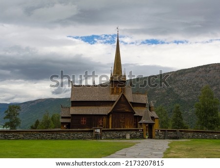 Lom viking medieval stave church in Lom Norway. Old wooden walls and tower, green lawn and grey stone fence, mountain slope and blue sky with clouds on the background Stock fotó © 