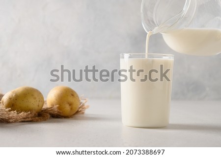 Pouring vegan potato milk in glass and potato in bowl on light background. Close up. Plant based milk replacer and lactose free.