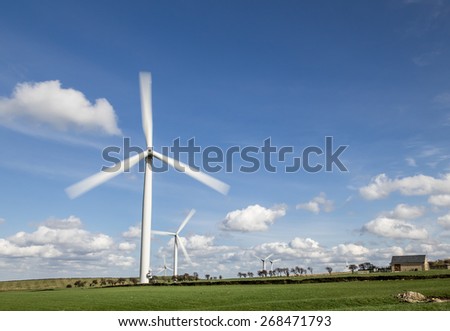 Wind Farm - Wind turbines in field with blue sky and clouds behind. Slow shutter speed to show movement of turbine.