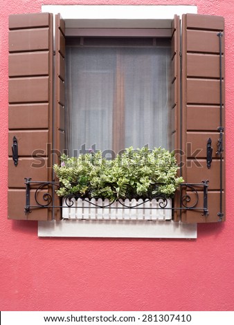 Burano, Italy - 21 May 2015: Red painted building. Close up of window shutters and plant box in window on one of the many different coloured painted buildings on the island of Burano near Venice