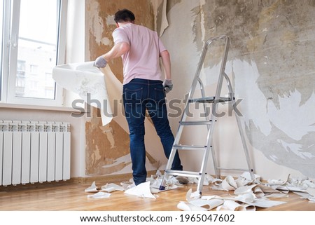 Caucasian man tearing off old wallpaper from wall preparing for home redecoration Imagine de stoc © 