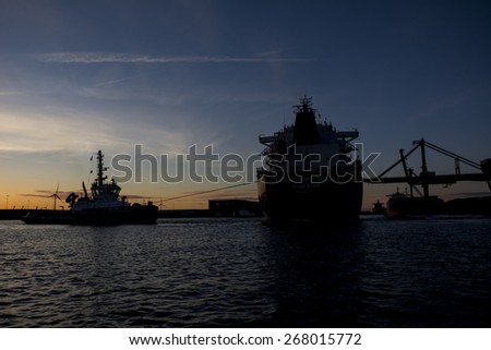 Port of Amsterdam, Noord-Holland/Netherlands - April 05-04-2015 - Tugboat Triton is connected to motor vessel Grand Ann Belle and assisting with departure. Photo taken during sunset.