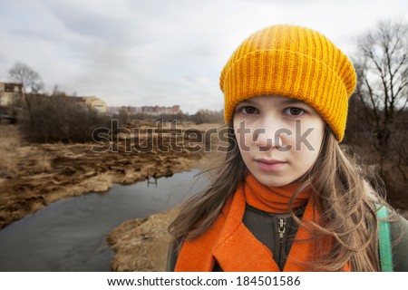 Pensive Teenager in orange knitte? hat and scarf stand alone near the scorched field. Spring time