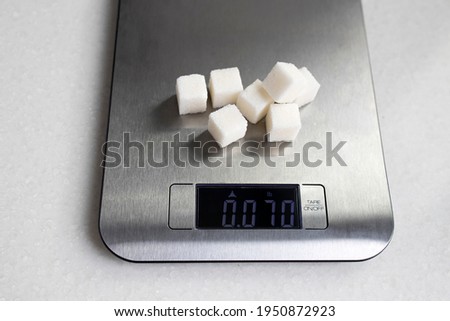 Seven lumps of refined sugar are weighed on a kitchen scale. Diet. Stock foto © 
