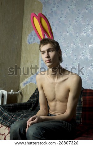 portrait of young cute thoughtful man with pirsing in eyebrow and rabbit`s ears. Man sitting on the sofa