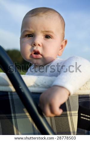 portrait of little cute boy six month old sitting on buggy. Park