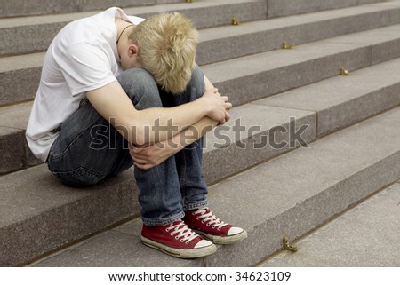 upset young blond man sitting on stairs laying his hand on his arm