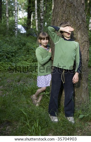boy close his eyes by hand. Girl look out tree. Hide-and-seek