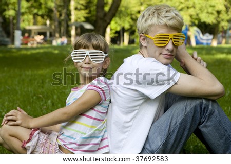 brother and sister in strange sunglasses sitting on grass in park
