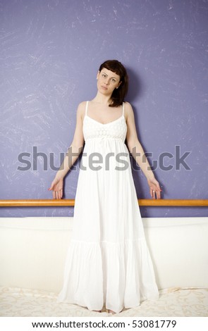 smiling flirting woman wearing white dress standing nearby lilac wall
