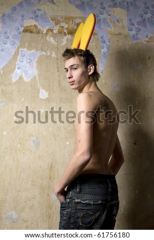young skinny man wearing rabbit ears standing nearby old wall