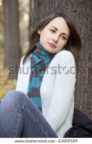 sad woman sitting nearby tree in autumn park