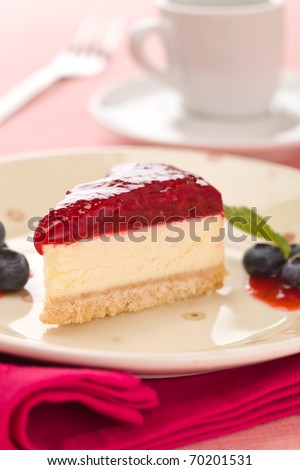 Piece of raspberry cheese cake in a plate with  fork and coffee cup in the background. Extremely shallow depth of field.
