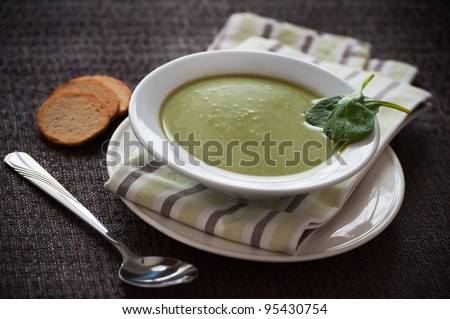 Vegetarian spinach cream soup on a dark background. Leaves and bread on the side.