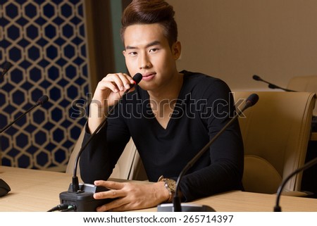 a portrait a man sit on the chair with microphone  on the table