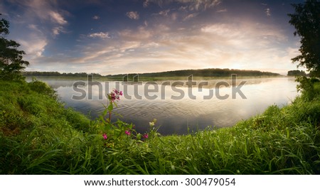 Fantastic foggy river with flowers and fresh green grass in the sunlight. Sun beams through tree. Dramatic colorful scenery, Russia. Beauty world.