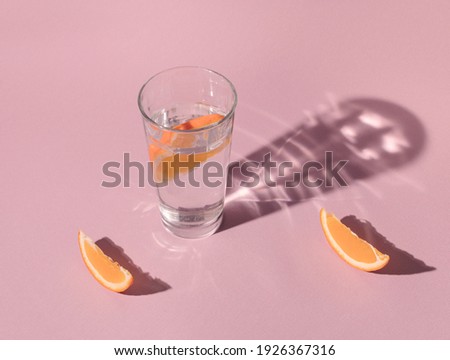 Glass of water and sliced lemon and orange on pink background with fancy shadows 商業照片 © 