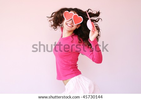 Beautiful young woman in heart-shaped glasses caught in jump motion with paper heart in hand