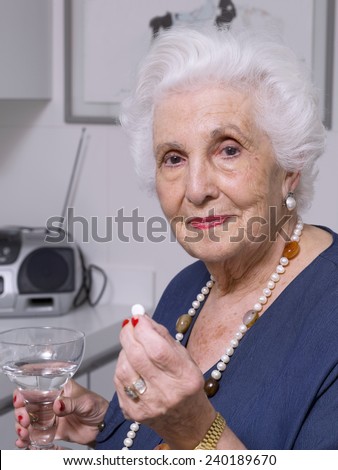 Close up of an elderly woman in the kitchen, taking a medicine