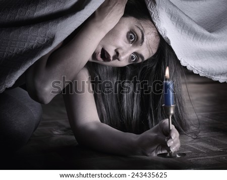 A young woman with fear, looking under the bed and surprised at what she sees