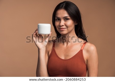 Portrait of attractive woman holding container with face cream and positively looking at camera, isolated on beige color background Foto stock © 