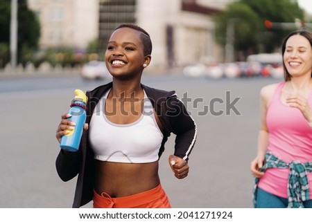 Cheerful smiling friends in sportswear running in the city dicussing. Multiethnic women having a fitness workout. 商業照片 © 