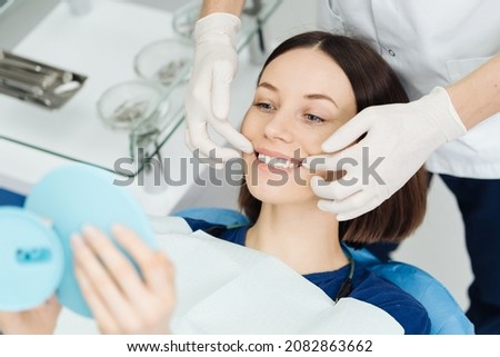 Look at me. Attractive caucasian lady checking her beautiful smile in mirror after stomatological treatment. Satisfaction of the visit stomatologist Foto stock © 