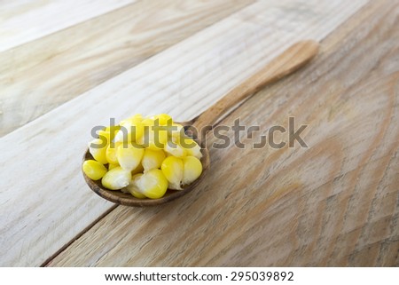 Yellow corn in a wooden spoon / kernels on wooden spoon isolated on wood background.