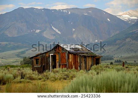 Old cabin in field with mountains in the background