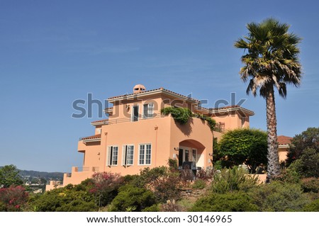 House surrounded by trees and blue sky. Orange color. Large palm tree in the back. Patio area in back.