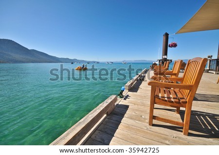 A group of wooden chairs lined up on a dock facing the lake
