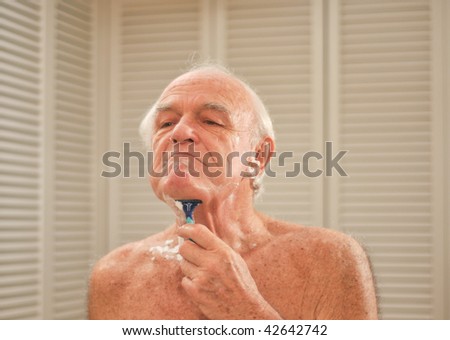 Elderly man shaves in front of a mirror.