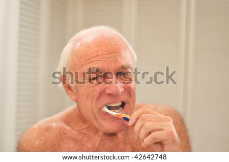 Elderly man brushes his teeth  in front of a mirror.
