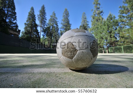 Soccer ball on a tennis court surrounded by trees