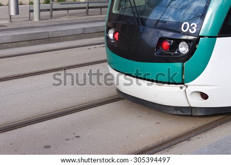 Close-up of a modern green and white tram in the rails. Detail of the lights, a number three and the driver cab of the streetcar stopped in the tramway station.