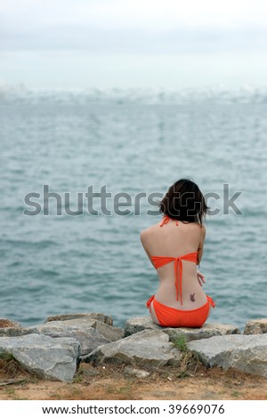 Bikini girl with butterfly tattoo sitting on beach looking at sea