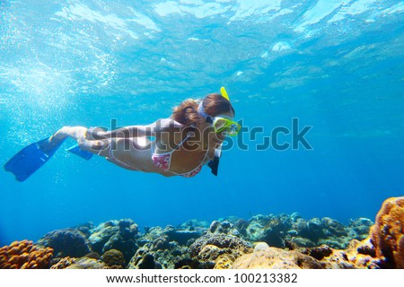 Young woman diving on a breath hold and fining over coral reef in blue transparent sea