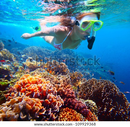 Woman with mask snorkeling in clear water over vivid coral reef