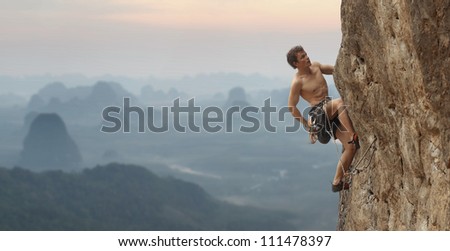 Young man climbing vertical wall with blurred valley view on the background