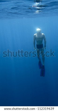 Underwater shoot of a young athlete finning from a depth to surface on a breath hold