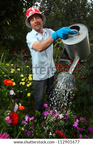 Mature caucasian man watering green garden with a lot of flowers