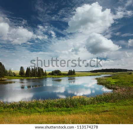 Summer river with green meadows around and blue cloudy sky