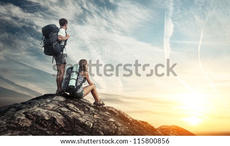 Two tourists with backpacks enjoying sunset on top of a mountain