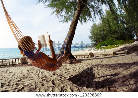 Young woman reading a book lying in a hammock on tropical sandy beach